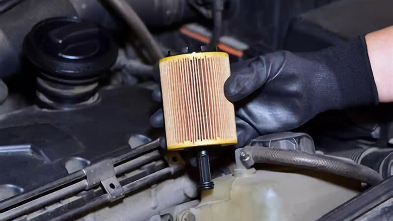 How to install an oil filter, a hand holding a filter above an engine bay