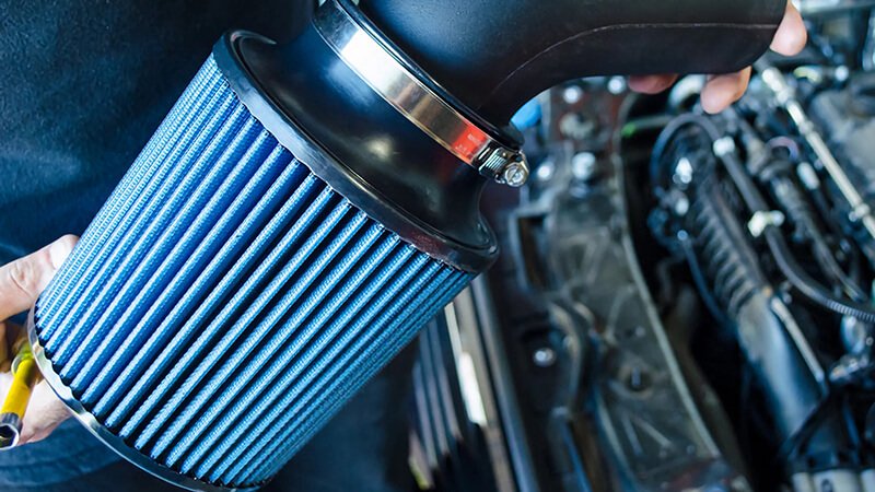 Blue air filter held in hand, installed in a vehicle